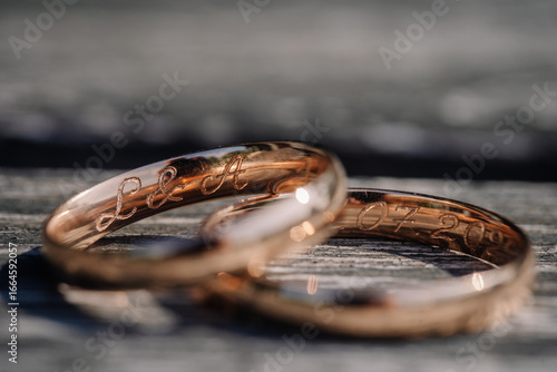Tableau sur toile Close-up of two engraved gold wedding rings resting on wooden surface, with initials “L & A” and a date visible, symbolizing love and commitment
