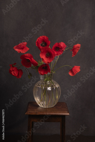 still life with red poppies in glass vase on stool in dark painterly renaissance style