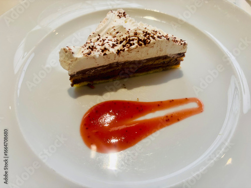Slice of layered chocolate and cream cake served on a white plate with a decorative smear of bright red strawberry sauce