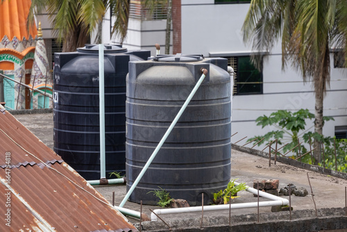 Konstfotografi Two large black plastic water tanks sit on a residential rooftop in Bangladesh, connected by visible water pipes, showcasing an essential element of urban infrastructure