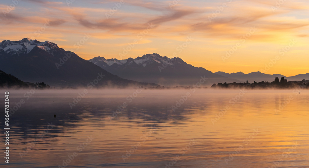 Sunrise over a misty lake with snow-capped mountains in the distance. Sunrise over a misty lake with snow-capped mountains in the distance.