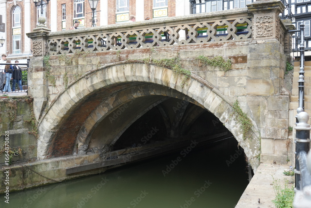 Obraz premium Lincoln, Lincolnshire, England - August 21 2025: Medieval stone bridge over river with historic architecture.