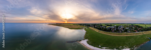 Serene beauty of a small beach on Markermeer lake in Schellinkhout the Netherlands during sunset. The tranquil scene features lush meadows, houses, and the gentle evening light. Aerial Panoramic view
