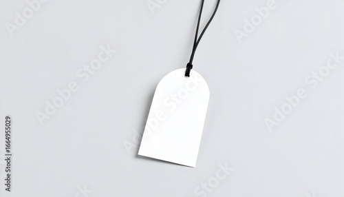 Clean and minimalist mockup of a blank white clothing tag with an arched top, hanging from a black string on a neutral grey background.