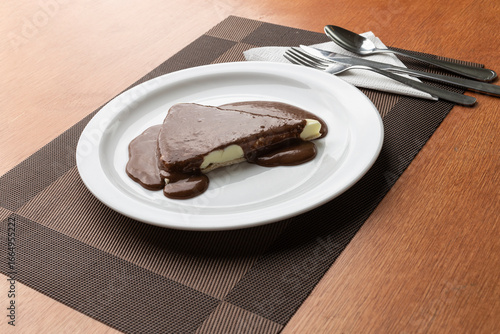 Pizza doce de sorvete de baunilha com calda de chocolate, servido em um prato branco em uma mesa de madeira.