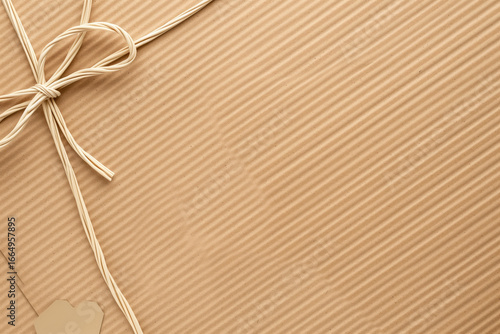 Kraft paper gift wrap with raffia bow and blank tag — diagonal ribbed texture, warm tan background