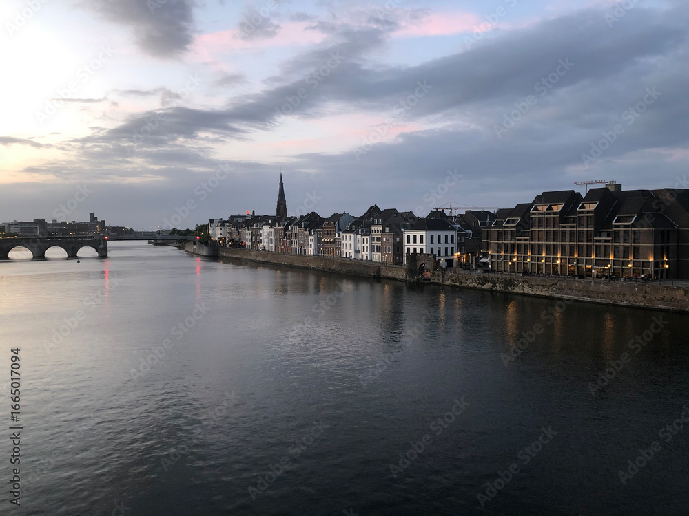Fototapeta premium Eastern View of Maastricht with the Meuse and Historic Stone Bridge – Dutch Architecture, Calm River, and Clear Sky Reflect the Timeless Charm of Limburg’s Capital in the Heart of the Netherlands