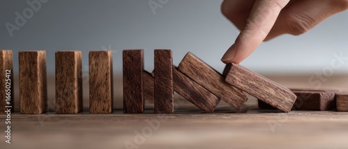 The domino being stopped by a human finger preventing a cascading wooden block fall