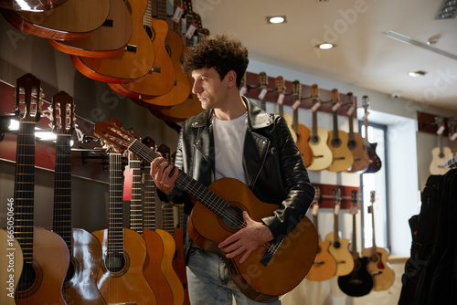 A man in a stylish leather jacket holds an acoustic guitar