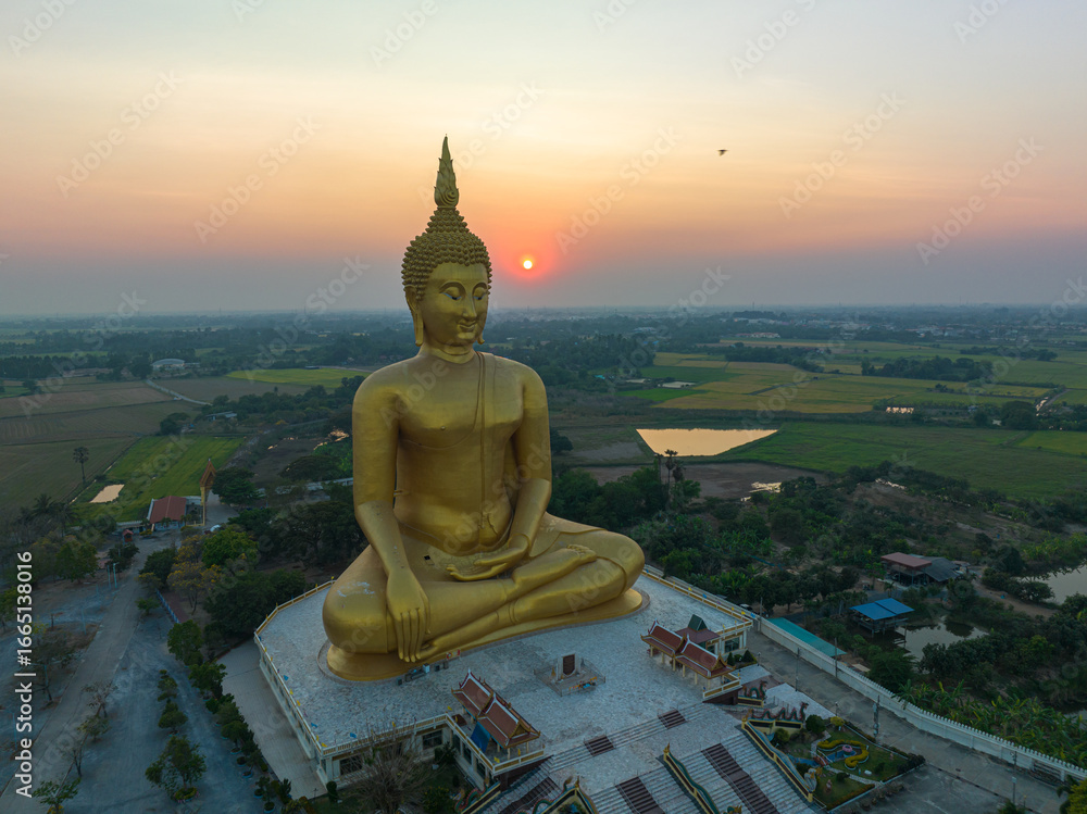Obraz premium scenery sunset behind the great golden Buddha landmark of Thailand at wat Muang Ang Thong Thailand. The largest Buddha statue in the world Surrounded by rice fields. colorful sky background.