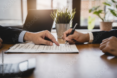 Fototapeta Naklejka Na Ścianę i Meble -  businessman sitting at desk holds pen signing contract paper, lease mortgage, employment hr or affirm partnership