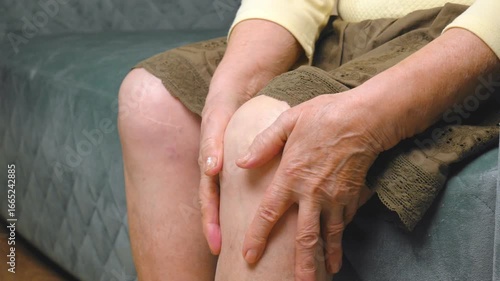 The hands of an old elderly woman massage an injured knee or joint, leg pain, discomfort from injury, osteoporosis or arthritis, cannot walk due to pain, cramps, rheumatism