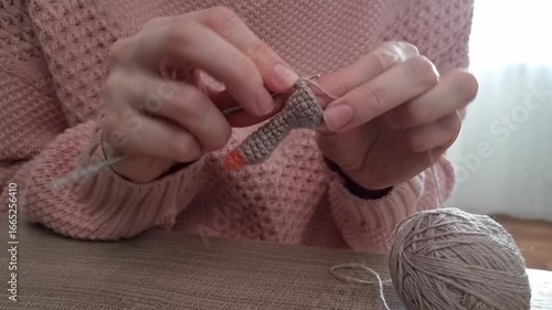 Women 's hands are crocheting a small toy . Hands holding a hook and a knitted product are visible nearby.