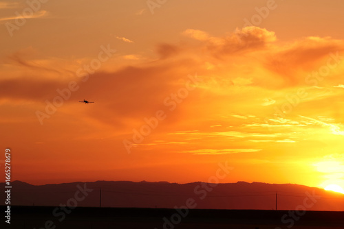 The silhouette of an airplane flying in the rays of the red sun setting on the horizon