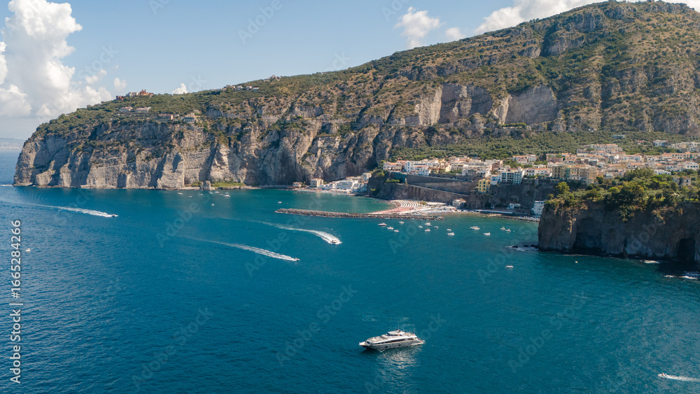 Fototapeta premium Aerial photo of Meta di Sorrento and Piano di Sorrento seen from the sea, with the Sorrento coast shining under the summer sun. A stunning seaside view of cliffs, beaches, and blue waters. Italy.