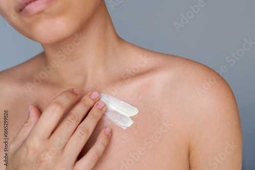 Close-up of a young woman applying moisturizing cream to her collarbone area. Natural skincare routine, body hydration, self-care and gentle feminine touch on neutral background