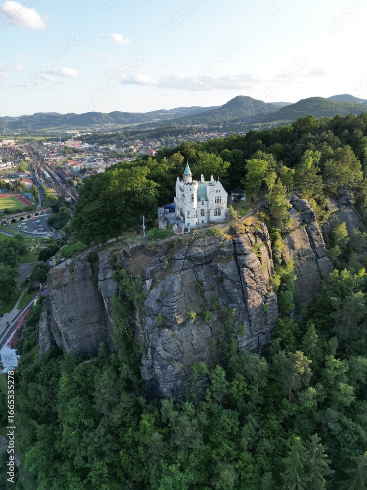 Obraz premium Aerial drone footage of the Pastyrska Stena lookout tower in Decin, Czech Republic. Scenic panoramic views of the historic tower, sandstone cliffs, and the Elbe River surrounded by nature 