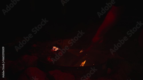 Person stirs embers in night campfire with wooden stick