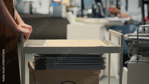 Картината върху платно Professional archivist uses rolling trolley to transport documents and records, assisting the ceo and coworkers with efficient handling of critical paperwork in a modern workplace