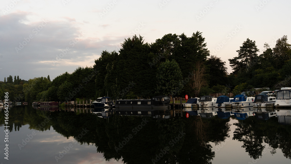 Fototapeta premium A serene scene of boats moored near a historic lock and dam architecture. Calm waters reflect the structures and vessels, capturing a peaceful moment of nautical life and industrial heritage.