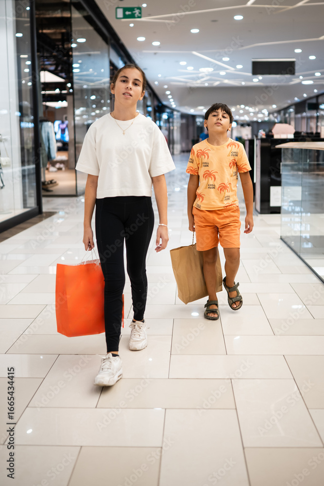 Obraz premium Teen girl and little boy walking in shopping mall with shopping bags