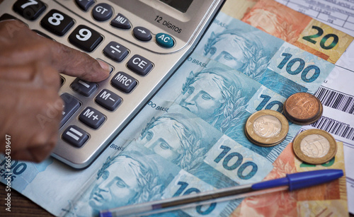 Brazilian currency. Brazilian reais notes on a table with a calculator, bills, and a pen. Concepts of economics, finance, Selic rate, taxes, IOF and financial planning