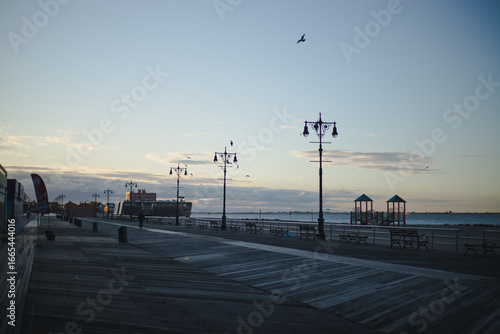 Wide view of a seaside boardwalk with street lamps and ocean horizon during sunset.