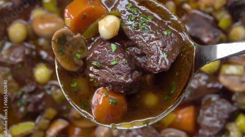 The ladle scoops up delicious pieces of beef bourguignon with vegetables, mushrooms and carrots top view. High quality 4k footage