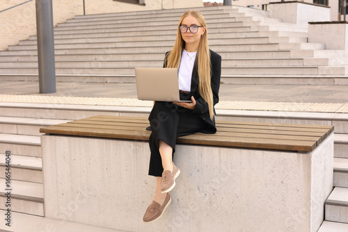 Young woman sitting on a wooden bench with a laptop on her lap. 