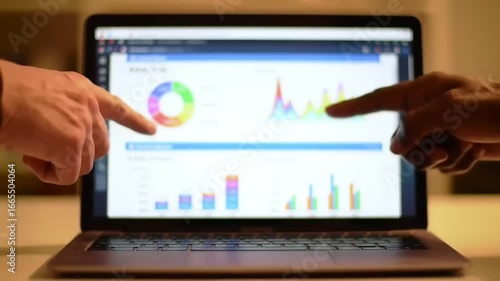 Two individuals analyzing data on a laptop screen, showcasing graphs and charts in an office setting