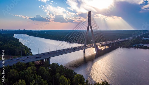 Aerial view of a cable-stayed bridge over a river at sunset with dramatic clouds and sunbeams