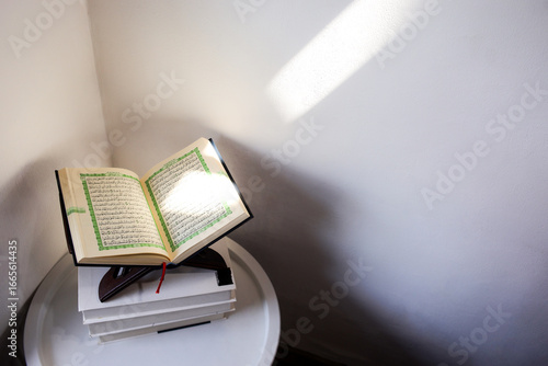 High Angle View Of Qur'an On Wooden Stand Placed On Stack Of Books Illuminated By Natural Sunlight