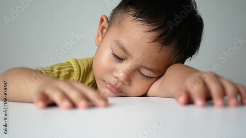 Asian little boy sleeping on a white table, accidentally sleeping without thinking much, on a white background, innocent little boy.