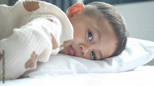 A big-eyed little boy was lying on the bed alone, refusing to get up