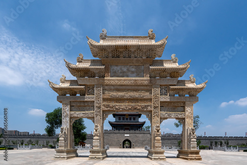 Ancient Chinese Stone Archway with Intricate Carvings Under Blue Sky