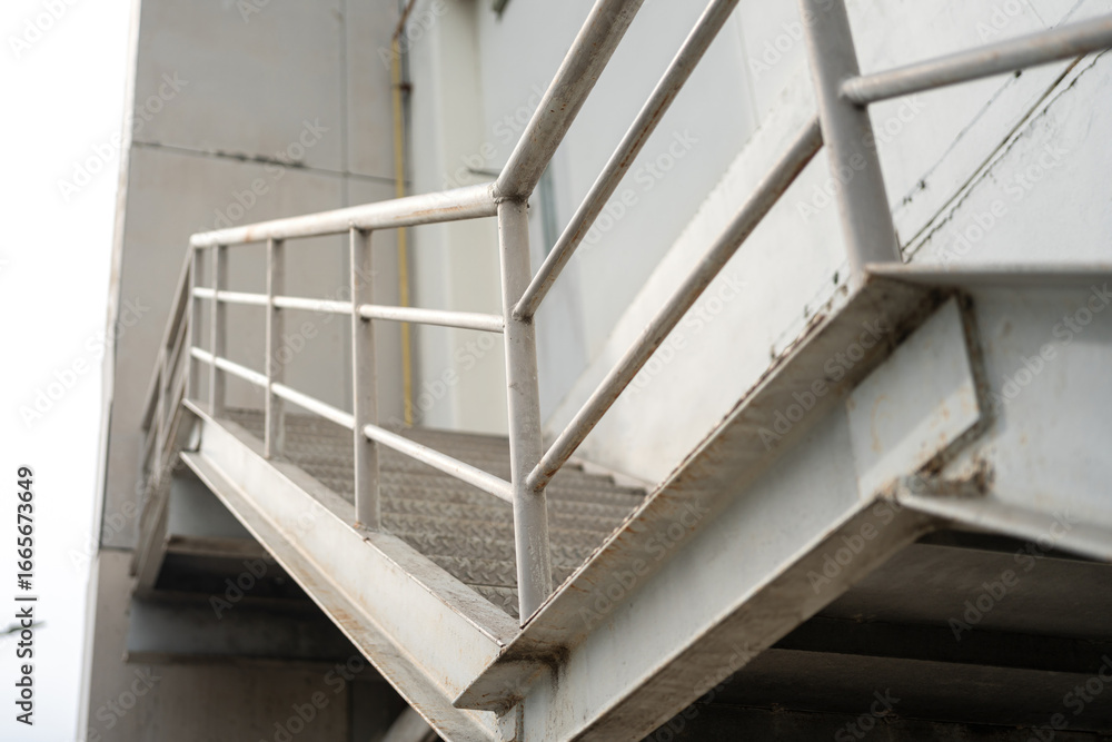 Fototapeta premium An emergency or evacuation stairway route, made from metal structure that located at outside of factory building. Building transportation part object, close-up with selective focus.