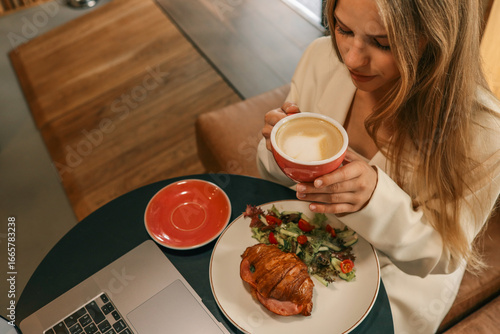 Foto Woman enjoying coffee with croissant and fresh salad at cozy cafe table, holding