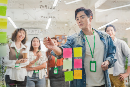Asian business creative marketing team brainstorming startup strategy using glassboard and sticky notes. Collaborative ideation session demonstrates design thinking methodology disruptive innovation