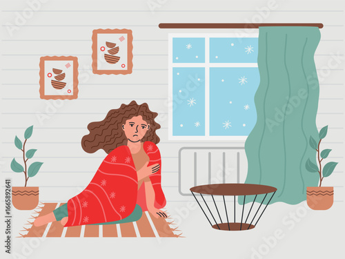 Woman freezes and sits near cold battery. Snow is outside the window, cold season.