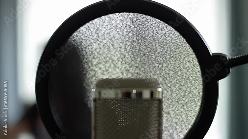 Studio microphone behind a black pop filter, close up, neutral colors, soft lighting