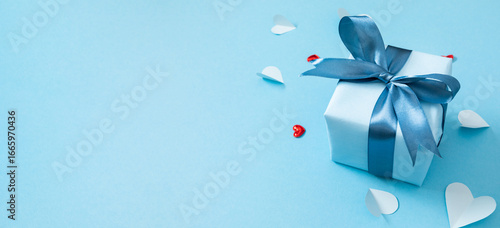 Festive composition with a blue gift and hearts on a pastel blue background.