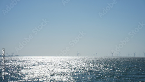 A scenic view of offshore wind turbines on a clear day with the sunlight reflecting off the ocean surface.It represents clean energy, environmental sustainability, and the future of renewable power.