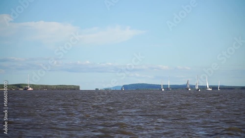 Sailboats are sailing on a lake. The sailboat is white . The sky is cloudy