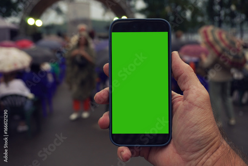Hand holding smartphone with green screen at outdoor event