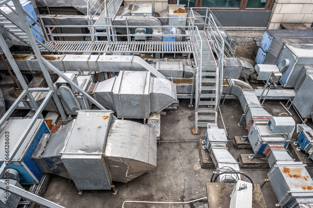 Fototapeta premium an industrial rooftop cluttered with various metallic ventilation systems, including large rectangular ducts and ladders
