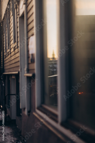 Wallpaper Mural The reflection of a distant church spire and a warm, golden sunset is visible in the window of a traditional wooden building in Tromsø, Norway, creating a blurry yet beautiful urban scene. Torontodigital.ca
