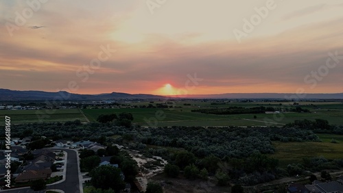 Aerial view of the setting sun casting a golden glow over the sprawling green fields and distant mountains, Nampa, Idaho, United States.