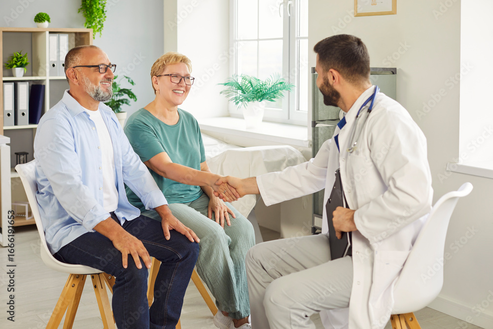 Obraz premium Smiling elderly senior couple meets a doctor in clinic for medical consultation, shaking hands as they discuss care options and treatment. Seniors greeting physician during exam. Medicine concept.