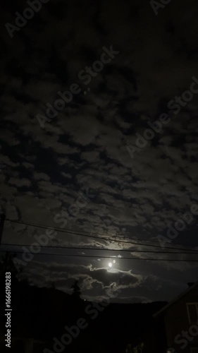 Moonlight illuminating dark cloudy night sky over mysterious landscape, dramatic nocturnal nature scene
