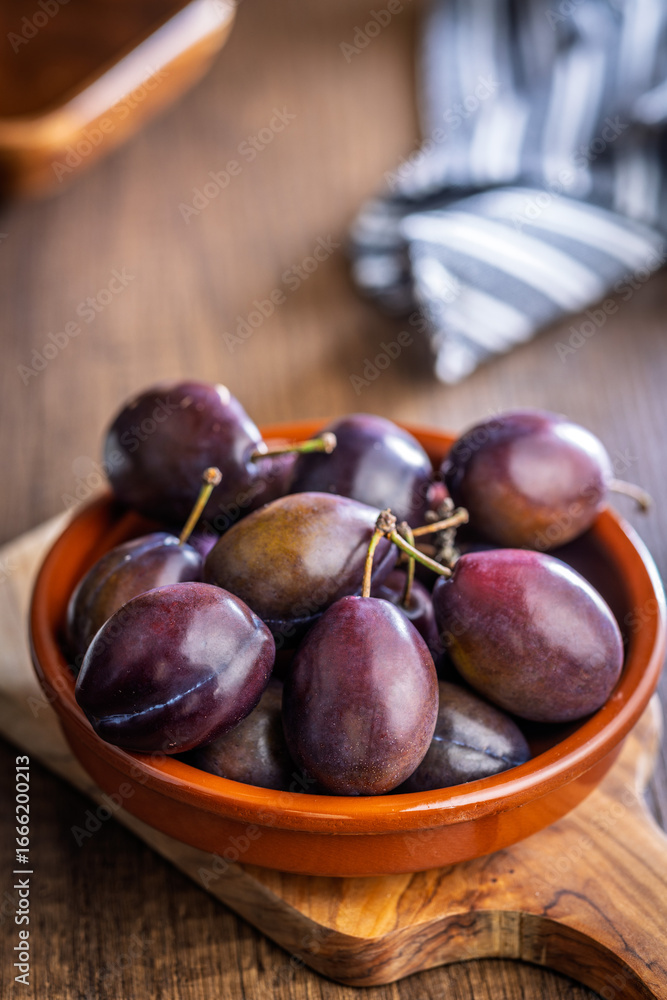 Obraz premium Ripe plums in bowl on wooden table.